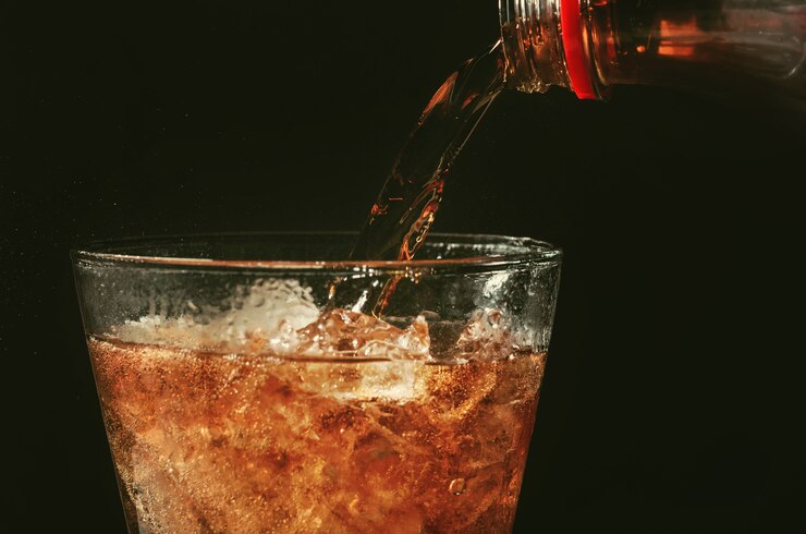 Um copo de vidro sendo preenchido com um refrigerante com cola.